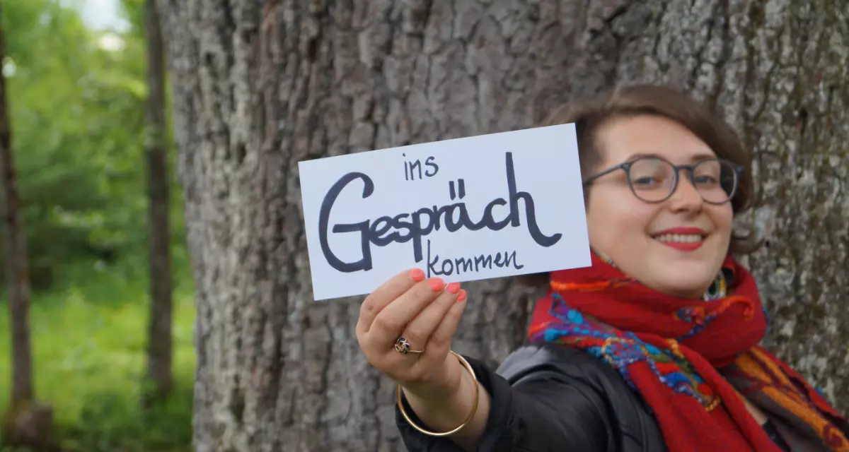 Teamerin beim Team meX mit Schild „Ins Gespräch kommen“. Foto: Team meX
